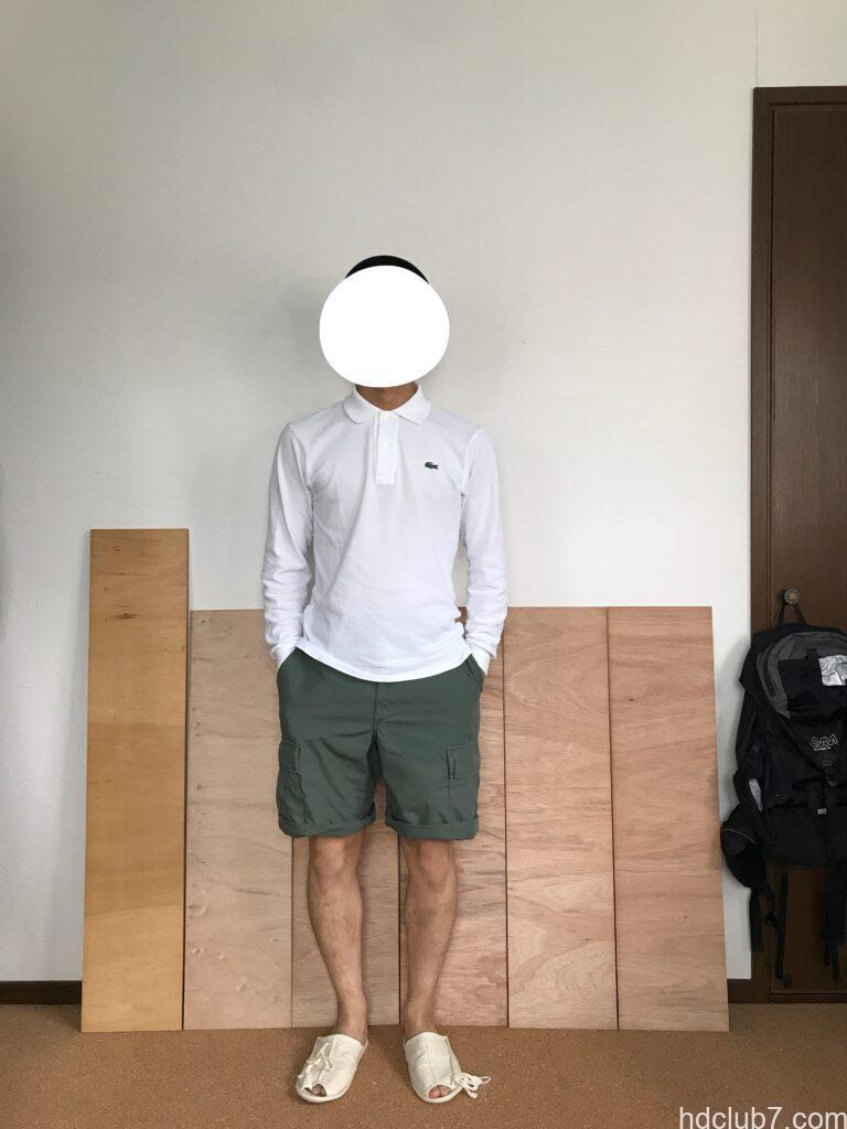 ロールアップしたプロッパーのBDUカーゴショーツとラコステの長袖ポロシャツを着て立っている男